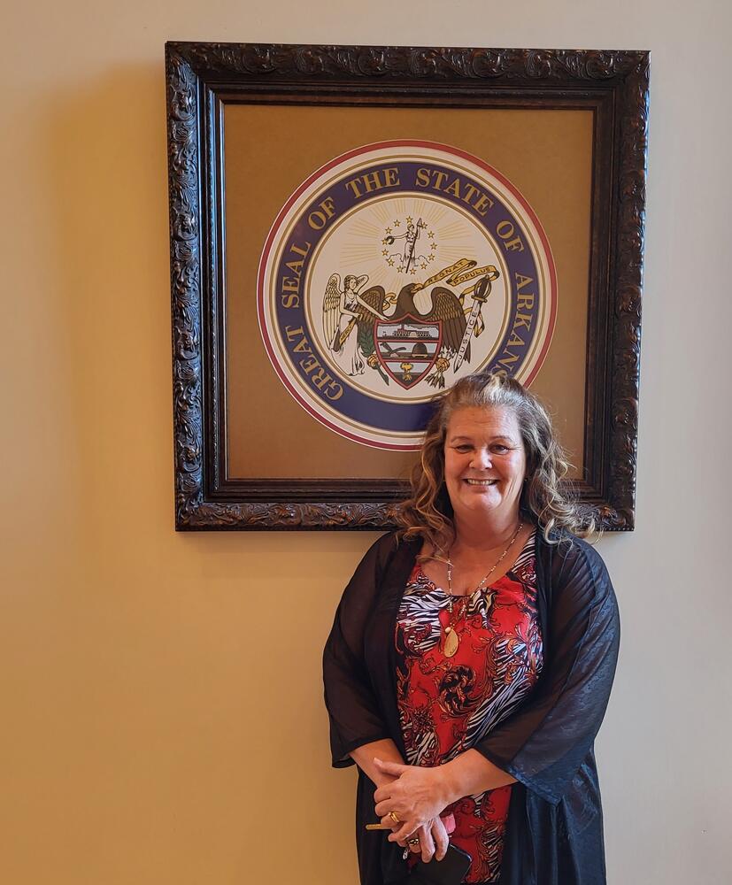 Lyna standing in front of State of Arkansas seal