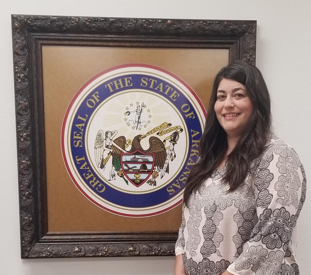 Beckie standing in front of State of Arkansas seal